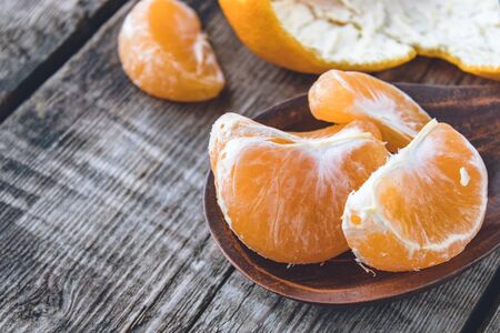 Slices of ripe yellow tangerine lie in a bowl near the tangerine peel on a wooden table. Citrus fruits, tangerines or oranges. Close-up.の写真素材