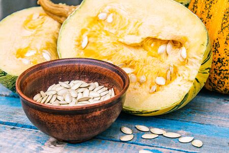 Pumpkin seeds in a bowl near a ripe pumpkin on blue old boards. Autumn harvest.の写真素材