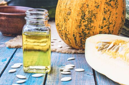 Pumpkin seed essential oil in a bottle near a pumpkin on blue old boards. Spa concept.の写真素材