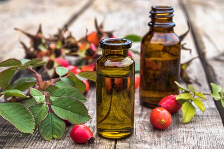 Glass bottle of rosehip seed essential oil with fresh fruits on a wooden table. Tincture or essential oil with rose hips. Spa herbal medicine.の写真素材