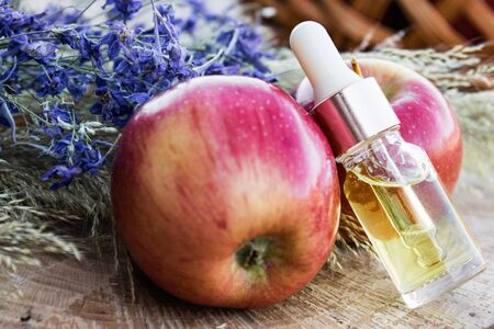 Glass bottle of apple essential oil near fresh apples on a wooden table. Essential oil is used to fill lamps, perfumes and in cosmetics. Close-up.の写真素材