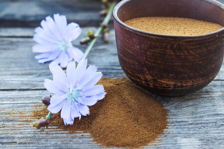 Blue chicory flower and a bowl of instant chicory powder on an old wooden table. Chicory powder. The concept of healthy eating a drink. Coffee substitute.の写真素材