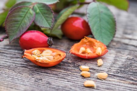 Red rosehips and cut berries in half with seeds on a wooden table. Close-up.の写真素材