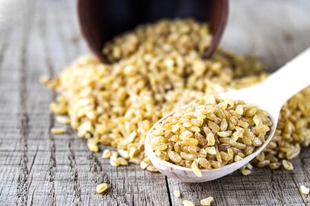 Dry bulgur grain in a wooden spoon. Healthy, dietary, vegan, gluten free product.の写真素材