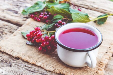 White mug or cup of hot viburnum tea on a wooden table next to red viburnum berries. Source of natural vitamins. Used in folk medicine. Close-up.の写真素材