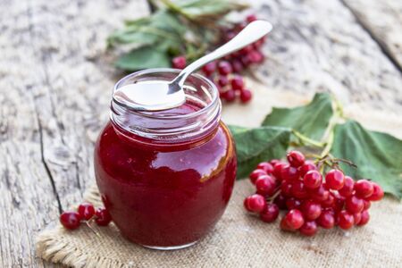 Glass jar of homemade viburnum jam with fresh viburnum berries on a wooden table. Source of natural vitamins. Used in folk medicine. Autumn harvest.の写真素材