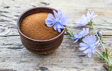 Blue chicory flower and a bowl of instant chicory powder on an old wooden table. Chicory powder. The concept of healthy eating a drink. Coffee substitute.の写真素材