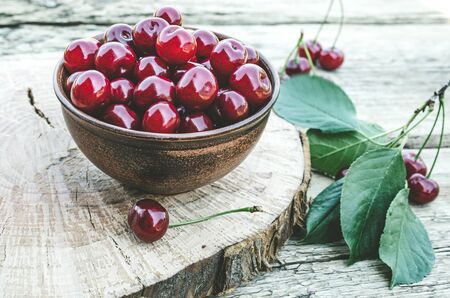 Red cherry in a bowl and green leaves on old wooden boards. Juicy delicious fruit. Close-up.の写真素材