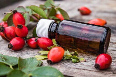 Rosehip seed essential oil in a bottle near ripe red rosehip berries. Tincture or essential oil with rose hips. Spa herbal medicine.の写真素材