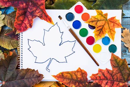 Colorful autumn leaves and paint for painting near white paper with place for text. Background with autumn leaves. Copy space for inscription. School conceptの写真素材