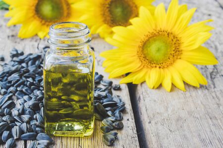 Sunflower oil in a glass jar with seeds and fresh flowers on a wooden background. Healthy foods and fats. Organic and eco food.の写真素材
