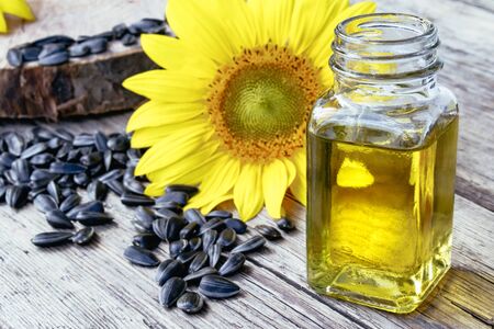 Sunflower oil in a glass jar with seeds and fresh flowers on a wooden background. Healthy foods and fats. Organic and eco food.の写真素材
