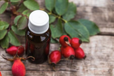 Rosehip essential oil on a wooden table near ripe red rosehip berries. Tincture or essential oil with rose hips. Spa herbal medicine.の写真素材