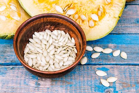 Pumpkin seeds in a bowl near a ripe pumpkin on blue old boards. Autumn harvest.の写真素材