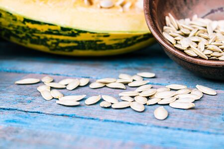 Pumpkin seeds in a bowl near a ripe pumpkin on blue old boards. Autumn harvest.