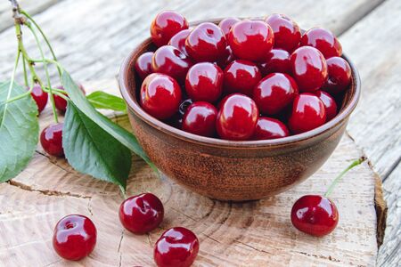 Red cherry in a bowl and green leaves on old wooden boards. Juicy delicious fruit. Close-up.の写真素材