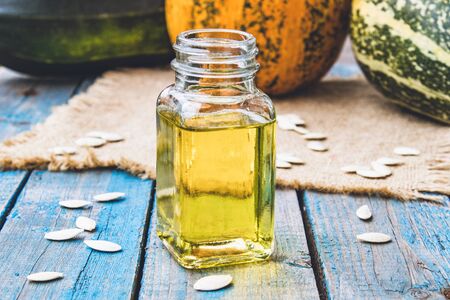 Pumpkin seeds and essential oil in a bottle near the pumpkin on blue old boards. Spa concept.の写真素材
