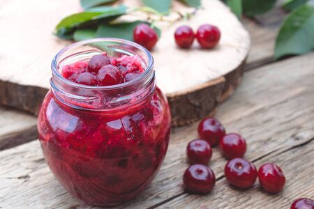 Fresh cherry jelly with fruit on a wooden background near the berries and green leaves. Close-up.