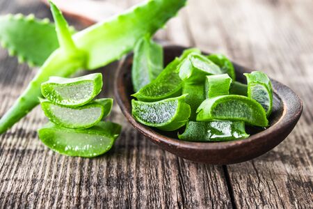 Fresh aloe vera leaves and slices of aloe vera in a spoon on a wooden background. Aloe for treatment and skin care.の写真素材