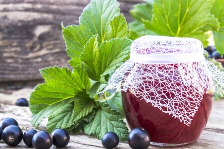 Black currant jam on the background of old boards near the green leaves and berries of currants. Natural currant jam. Close-up.の写真素材