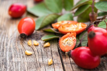 Fresh red rose hips and ripened berries in half with seeds on a wooden table. Close-up.の写真素材