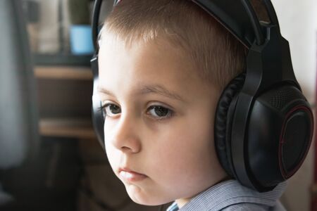 A sad or thoughtful boy is listening to music on headphones. Close-up of a baby's face.の写真素材