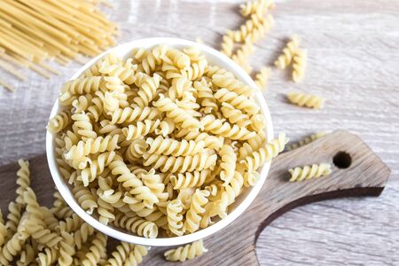 Dry pasta in a bowl on a cutting board on a light table background. Healthy eating or healthy lifestyle.の写真素材