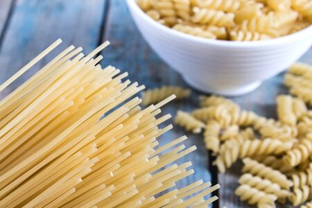 Dry pasta in a bowl on a background of blue boards near a pile of different pasta. Healthy eating or healthy lifestyle.の写真素材