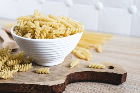 Dry pasta in a bowl on a cutting board on a light table background. Healthy eating or healthy lifestyle.の写真素材