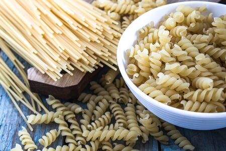 Dry pasta in a bowl on a background of blue boards near a pile of different pasta. Healthy eating or healthy lifestyle.の写真素材