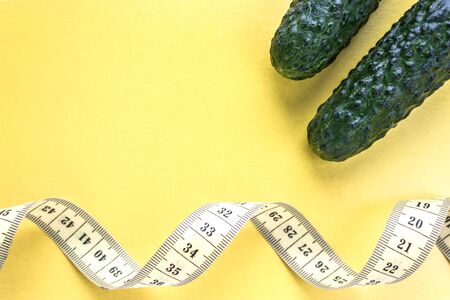 Fresh green cucumbers and yellow measuring tape on a yellow background, place for text. Healthy eating conceptの写真素材