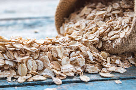 Gray oatmeal is scattered from the bag against the background of blue boards. The concept of a...