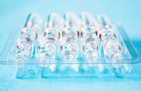 Medical ampoules on the table in transparent packaging on a blue background. Medical glass ampoules close up.の写真素材