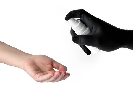 The hand of one person in a black latex glove sprays a disinfectant on the hands of another...
