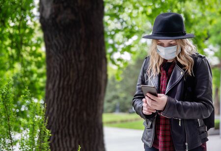 A young woman with blonde hair in a hat looks at the phone on the street.の写真素材