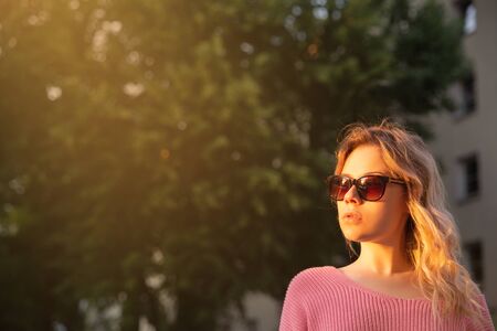 young woman in sunglasses and pink sweater outdoors in the eveningの写真素材