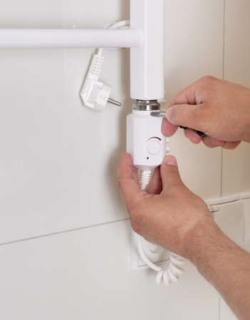 Male hands of a worker with a screwdriver. Plumber sets a heated towel rail.の写真素材