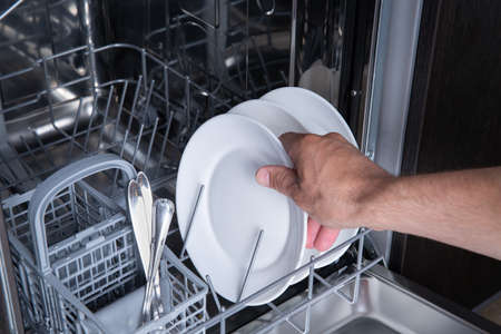 Housework open the dishwasher and the person puts the plate in the machineの写真素材