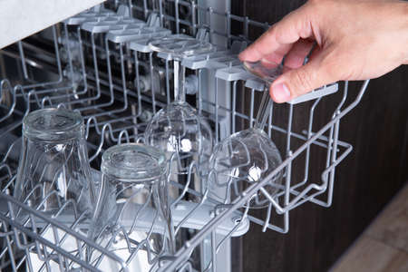 Housework open dishwasher and man putting a glass in the machineの写真素材