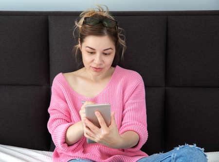 A beautiful girl is sitting in pink sweater with a phone , chatting.の写真素材