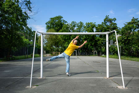 a gray-haired man catches an imaginary ball in a soccer goalの写真素材