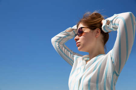 blonde in glasses and a light shirt against a blue skyの写真素材