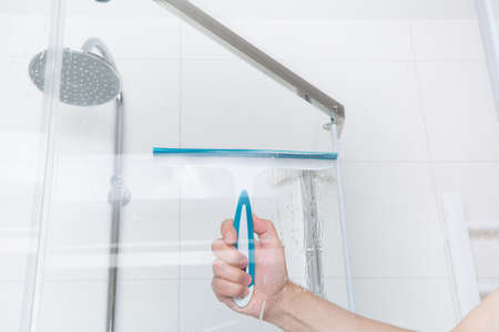 hand with glass scraper cleans glass in showerの写真素材