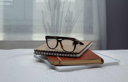 An image of a notebook and books placed in bed with glasses .blurred backgroundの写真素材