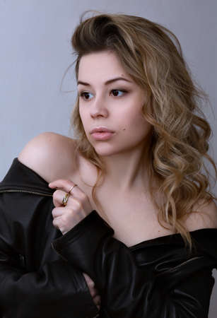 young blonde curly girl with bare shoulders in a leather jacket.の写真素材