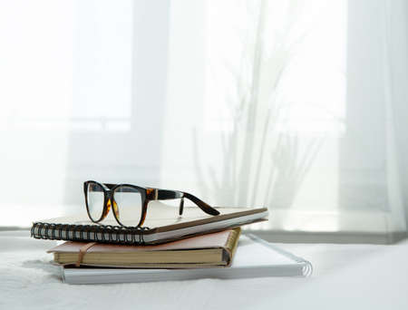 An image of a notebook and books placed in bed with glasses .blurred backgroundの写真素材