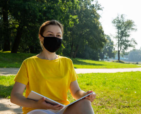 Image of a female student wearing a black protective mask sitting in a parkの写真素材