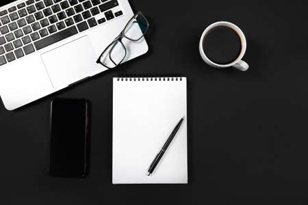 Black office desk with laptop, smartphone, pen, glasses and a cup of coffee.の写真素材