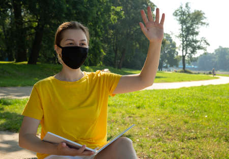 image of a smiling young woman in a black protective mask waving her handの写真素材