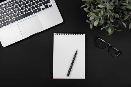Black office desk with laptop, smartphone, notebook and pen. Top view